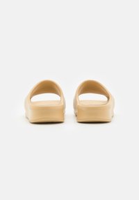 Zuecos ligeros beige con parte trasera abierta y forma redondeada, fabricados con un material suave y flexible. Plantilla texturizada para mayor confort.