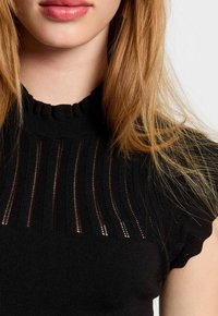 Black knitted top featuring a high neckline, short ruffled sleeves, and vertical cutout details in the fabric, creating a textured look.