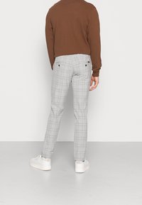 Grå rutiga byxor med slim fit, som har subtila rutmönster, bakfickor och en mjuk tygtextur, kombinerade med vita sneakers.