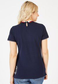T-shirt en coton bleu marine avec un col en contraste rouge et blanc, un petit trou en boucle dans le dos et des détails brodés près de l'ourlet.