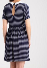 Marinblå klänning med vita horisontella ränder, korta ärmar, samlad midja, vit krage och droppformad skärning bak på en person som vänder ryggen mot oss.