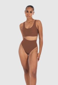 Conjunto de ropa deportiva marrón que incluye un top corto sin mangas y una braguita de bikini de talle alto. Textura suave y color sólido, diseño minimalista.