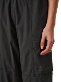 Close-up af en hånd, der hviler nær sidelommen på sorte bukser med teksten "HALO 1988|972|981" trykt på stoffet.