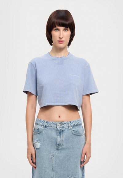 Blue cropped t-shirt with short sleeves and a slightly distressed neckline, paired with a light denim skirt featuring frayed edges and rips.