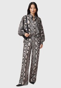 Ensemble deux pièces comprenant une chemise à manches longues et à boutons et un pantalon large arborant un motif serpent noir et beige, accompagné d'un sac noir.