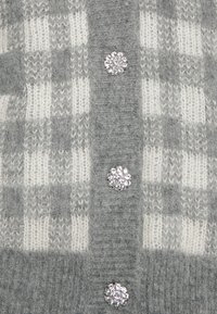 Grå och vit rutigt cardigan gjort av mjukt material, med dekorativa runda kristallknappar och en texturerad stickad mönster.