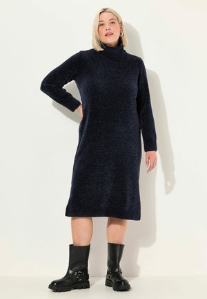 Robe col roulé en maille marine avec des manches longues, des poignets côtelés et un ourlet. Associée à des bottes épaisses noires avec des détails de sangle et de boucle.