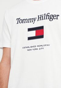 Hvid bomulds t-shirt med marineblå broderet mærkenavn "Tommy Hilfiger" og et flaglogo i røde, hvide og blå farver.