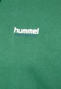 Grön sweatshirt med ribbad struktur, med en djärv vit och lila "hummel"-logotyp och "SPORTSWEAR" under den.