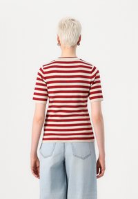 Top corto a maniche corte a righe rosse e beige con scollatura tonda, texture liscia, abbinato a jeans a vita alta azzurri chiari.
