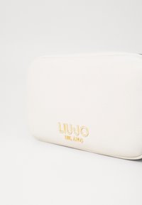 Portafoglio in pelle bianca texturizzata, di forma rettangolare. Presenta il logo del marchio "LIU•JO MILANO" in rilievo dorato sulla parte anteriore.