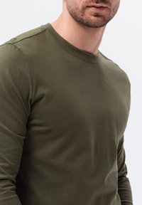 T-shirt a maniche lunghe, verde oliva, realizzato in cotone morbido. Presenta un collo rotondo e dettagli a costine sul colletto e sulle cuciture delle spalle.