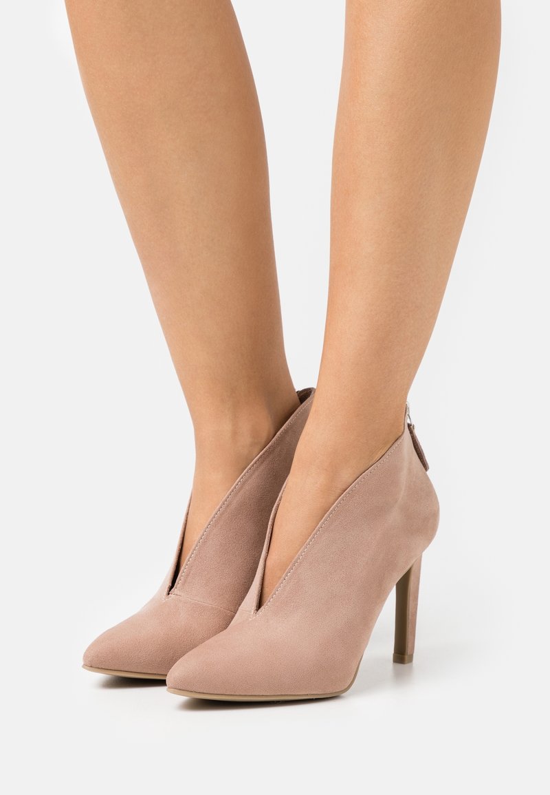 Zapatos de tacón alto de ante rosa con punta afilada, que presentan un diseño de corte profundo y un zipper trasero, expuestos sobre un fondo blanco.