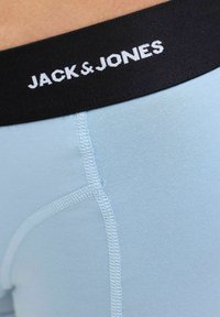 Himmelblaue Boxershorts mit einem schwarzen Bund, der "JACK & JONES" in weißen Buchstaben trägt. Glatte Stoffoberfläche und flache Nähte sind sichtbar.