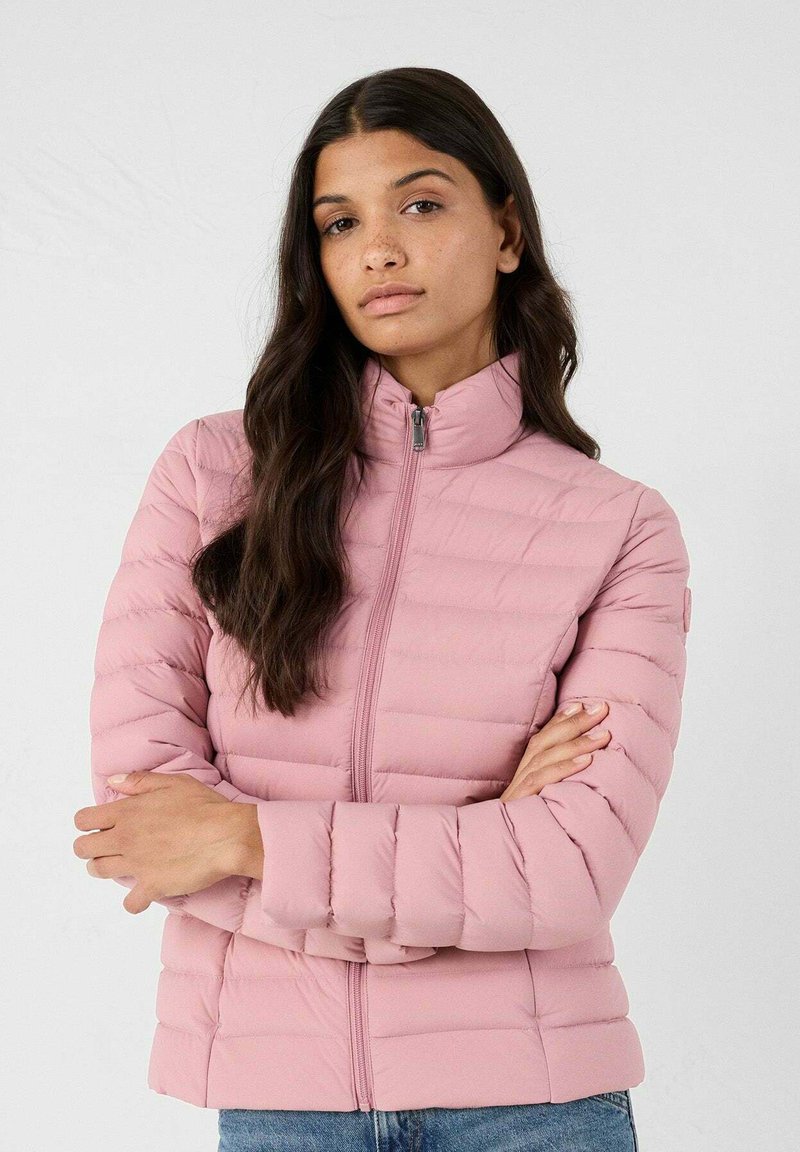 Chaqueta acolchada de color rosa claro con un cuello alto y cierre de cremallera, que presenta un diseño acolchado y una textura suave. Sin logotipos ni patrones visibles.