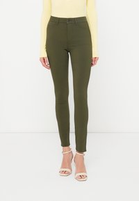 Κολάν σε ελιά πράσινο με ψηλή μέση, κατασκευασμένο από ελαστικό υλικό, με κλείσιμο μπροστά με κουμπιά και μήκος μέχρι τον αστράγαλο. Ορατές μπροστινές τσέπες.