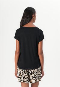 Black, short-sleeve t-shirt with a wide neckline, paired with beige shorts featuring a black and brown leopard print. Smooth fabric texture.