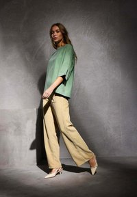 Un haut vert surdimensionné décontracté, un pantalon large beige à côtes et des mules à talons clairs. Un design minimaliste avec des textures douces et des couleurs neutres.
