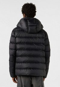 Zwarte pufferjas met horizontale doorgestikte secties, een capuchon en een gladde, glanzende stoftextuur. Volledige ritssluiting aan de voorkant.