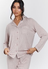 Conjunto de pijama rosa claro que incluye una camiseta de manga larga, cuello con solapa, cierre de botones en el frente y un bolsillo en el pecho con un borde blanco en contraste. Textura suave.