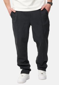 Schwarze, lässige Hose aus weichem Stoff, mit vorderen Taschen, sichtbaren Nähten und einem schmal zulaufenden Beinanschnitt, kombiniert mit weißen Sneakers.