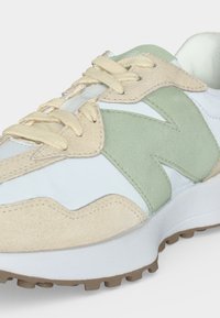 Baskets blanches avec des empiècements en daim beige, logo "N" en daim vert clair, lacets beiges et semelle en caoutchouc marron texturée.