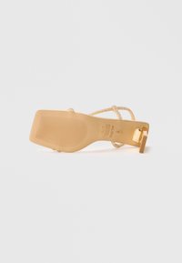 Beige high-heeled sandal with glittery straps, a textured sole, and a square block heel. Notable gold hardware accents on the strap.