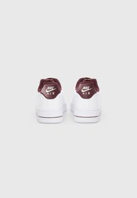 Bijele Nike Air tenisice s bordo detaljima, izrađene od glatke kože i s udobnom petom. Stražnji pogled naglašava brendiranje na tabanu petice.