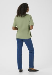 Vaaleanvihreä lyhythihainen paita sivuleikkauksella, yhdistettynä sinisiin slim fit -farkkuihin ja mustiin ballerinoihin. Sujuva rakenne, rento malli.