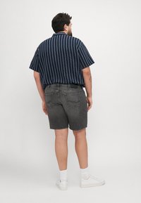 Kratke rokave mornarsko modra črtasta srajca, siva jeans kratka hlače, bele teniske in kratke nogavice. Zadnji pogled prikazuje sproščen kroj srajce in žepe kratkih hlač.