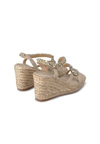Sandali con zeppa beige, dotati di suola in juta intrecciata, caratterizzati da cinghie incrociate e strass decorativi sul davanti. Texture liscia, design aperto.