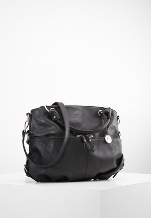 Sort læderhåndtaske med sølvdetaljer, dobbelte håndtag, en lynlåslomme foran og et rundt metal-logo vedhæng, der hviler på en hvid overflade.