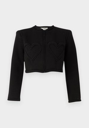 Veste noire courte à manches longues, présentant deux motifs en forme de cœur cousus sur le devant et une fermeture éclair à l'avant. Texture lisse.