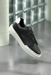 Μαύρα δερμάτινα αθλητικά παπούτσια με λευκές λαστιχένιες σόλες. Διαθέτουν ομαλή υφή, σχεδιασμό με κορδόνια και διακριτικό λογότυπο στο πλάι.