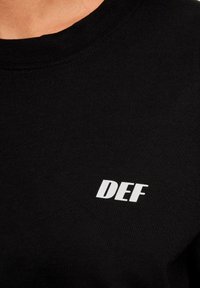 Black cotton sweatshirt featuring a round neckline and a white "DEF" logo printed on the chest. Smooth texture with visible stitching.