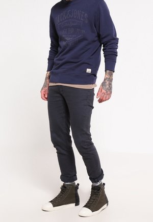 Marineblauwe sweatshirt met frontprint, gecombineerd met donkere jeans en groene hoge sneakers met witte zolen en zwarte accenten.