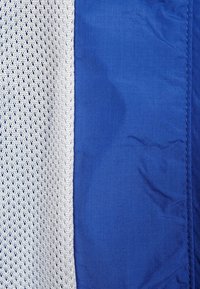 Blått tyg med en slät textur, intill ett nätmaterial i ljusgrått med små diamantformade hål, som skapar en kontrast i designen.