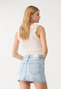Maglione bianco a maglia con motivo a diamante e colletto in pizzo abbinato a una mini gonna in denim blu chiaro con tasche posteriori.