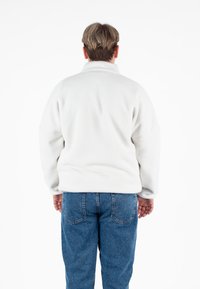 Biały polarowy pulower z wysokim kołnierzem, opuszczonymi ramionami i miękką teksturą, w połączeniu z niebieskimi jeansami.