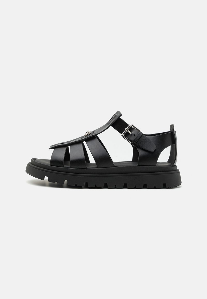 Black sandal featuring a strappy design, made of textured material, with a chunky sole and adjustable buckle for a secure fit.