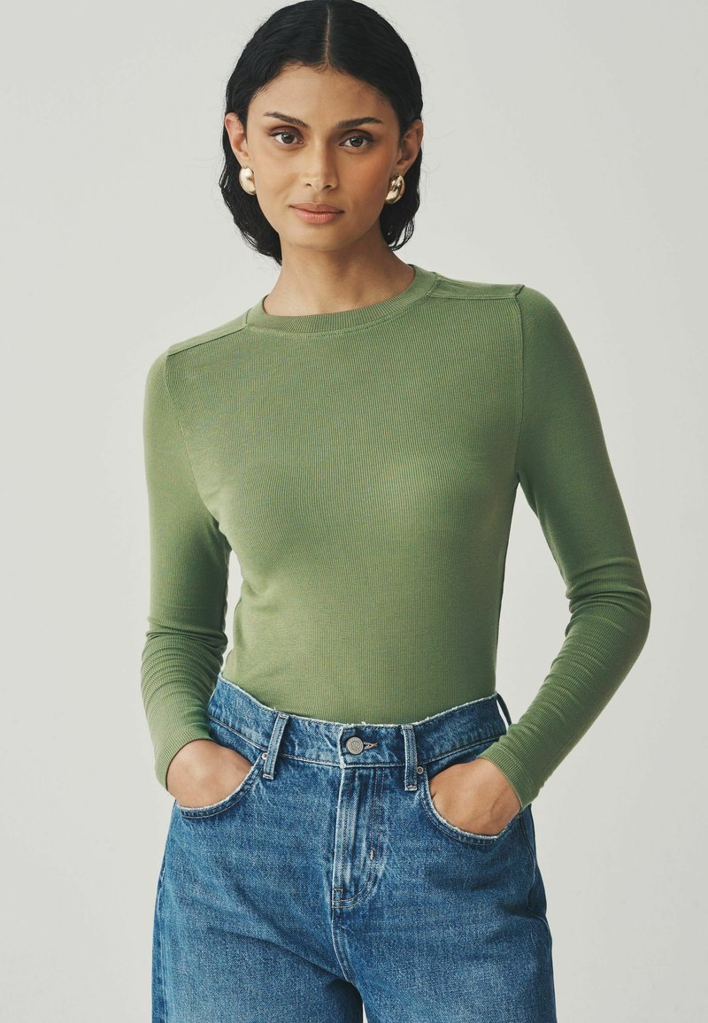 Long-sleeve, ribbed top in olive green paired with high-waisted blue jeans. The top features a crew neck and fitted silhouette.