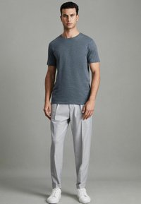 T-shirt gri cu mânecă scurtă, asortat cu pantaloni gri deschis și adidași albi. T-shirtul are o croială clasică; pantalonii sunt pliați și au manșete.