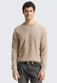 Hellbraunes, strukturiertes Sweatshirt mit Rundhalsausschnitt und langen Ärmeln, kombiniert mit dunkelgrauen Jeans und einem schwarzen Gürtel. Einfaches und lässiges Design.