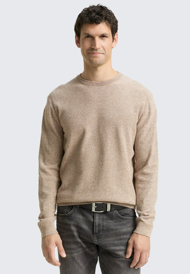 Hellbraunes, strukturiertes Sweatshirt mit Rundhalsausschnitt und langen Ärmeln, kombiniert mit dunkelgrauen Jeans und einem schwarzen Gürtel. Einfaches und lässiges Design.