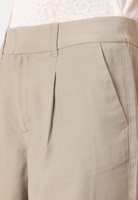 Béžové kalhoty s hladkou texturou, s plochým předním dílem, dvěma bočními kapsami a přiléhavým střihem s jemným nařasením.