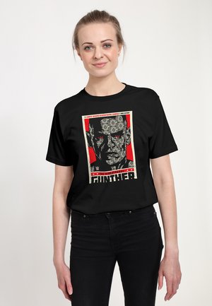 Sort bomulds-T-shirt med tryk af et ansigt i grå, omgivet af en rød kant med tekst øverst og nederst.