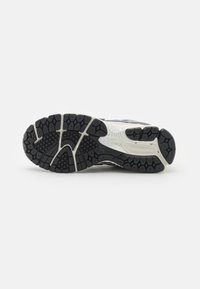 Suola di una scarpa da corsa New Balance bianca e nera che mostra un design del battistrada esagonale e decorato su uno sfondo bianco.