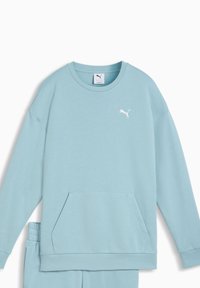 Világoskék hosszú ujjú pulóver, kerek nyakkivágással és első zsebbel. A mellrészen apró, fehér Puma logó található. Puha szövet textúra.