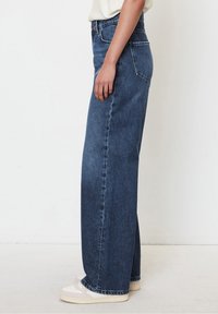 Wide-leg jeans in dark blue denim, featuring a high waist, five-pocket design, and a frayed hem. Paired with white sneakers.
