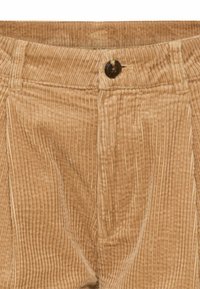 Tan corduroy broek met verticale ribbeltextuur, een frontale knoopsluiting en subtiele plooidetails.